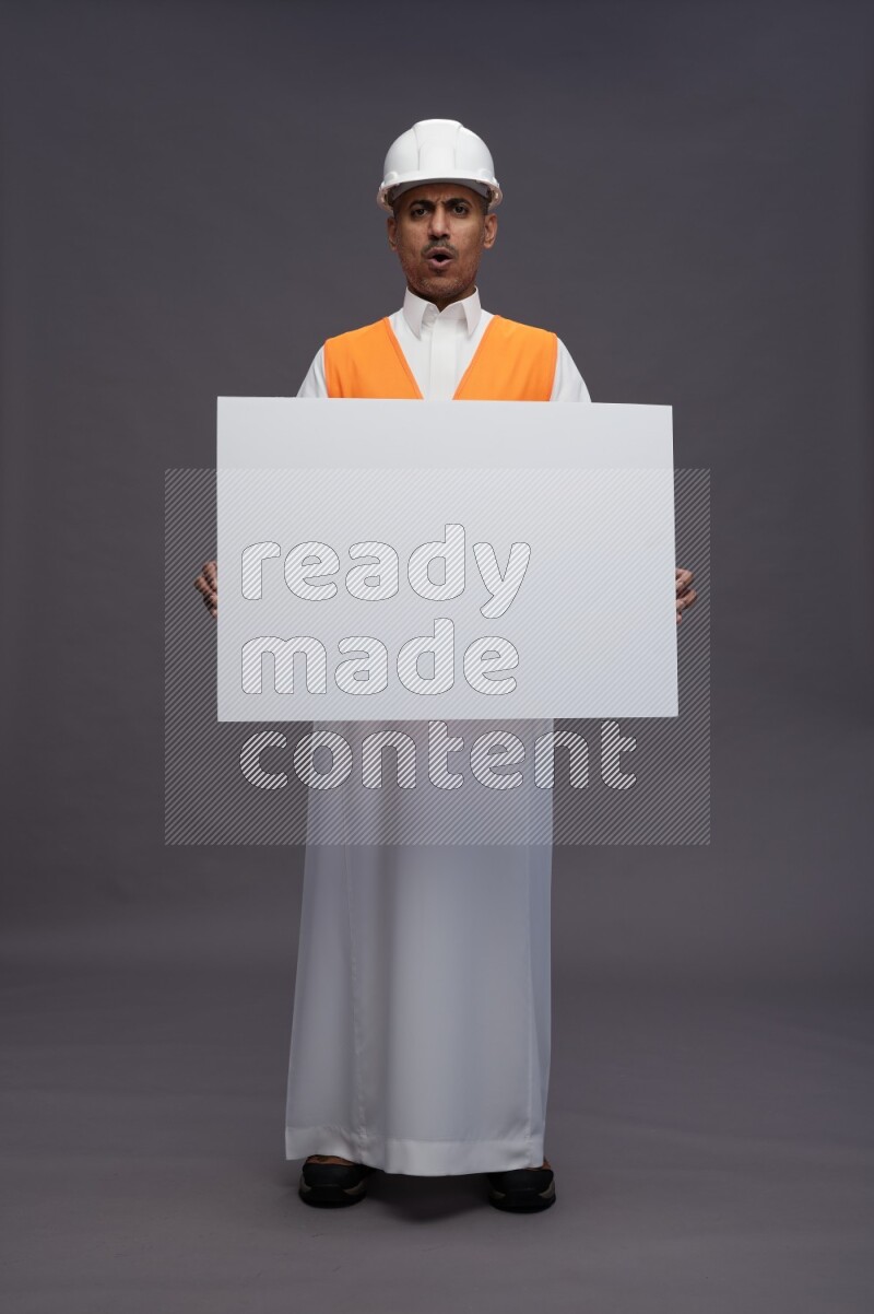 Saudi man wearing thob with engineer vest standing holding board on gray background