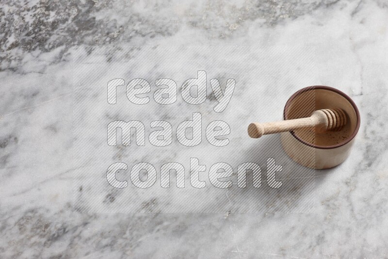 Beige Pottery oven bowl with wooden honey handle on the side with grey marble flooring, 65 degree angle