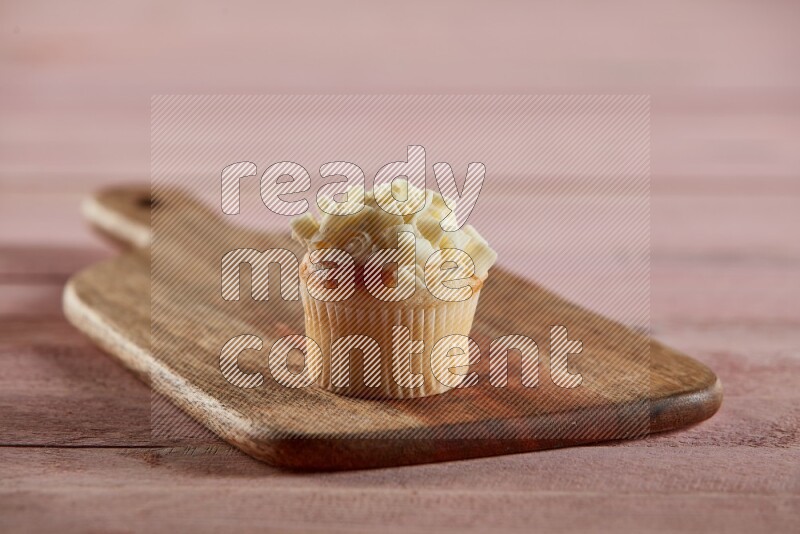 Vanilla mini cupcake topped with white chocolate curls on a wooden board