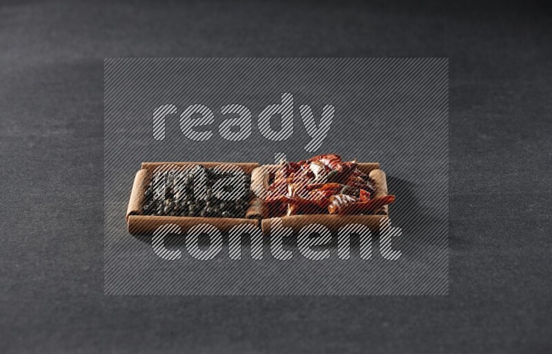 مربعان من أعواد القرفة ممتلئان بالفلفل الحار المجفف وحبوب الفلفل الأسود علي خلفية سوداء