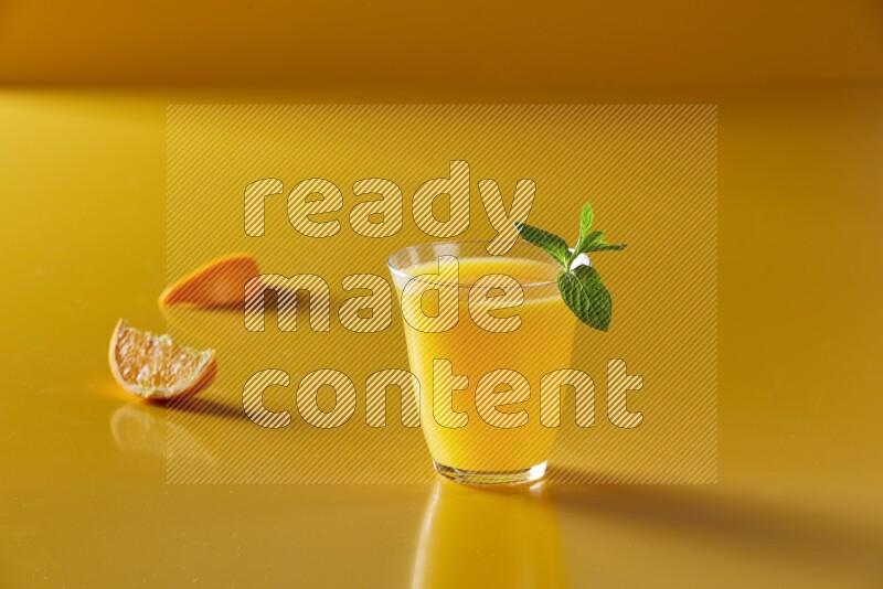 glass of orange juice with  mint on yellow background
