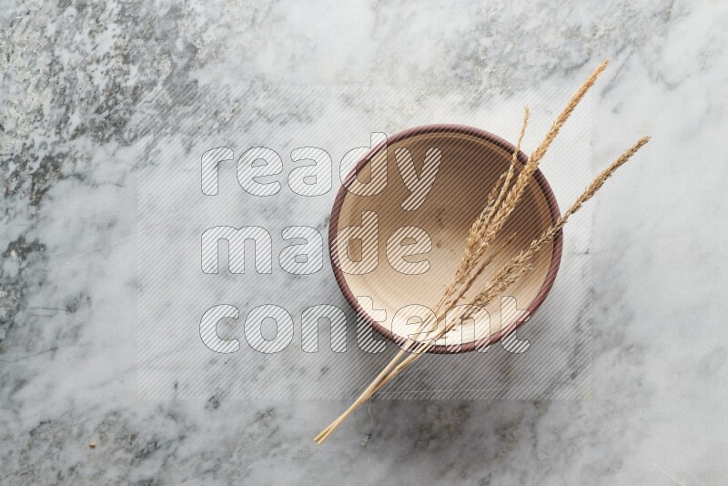 Wheat stalks on beige pottery oven bowl on grey marble background