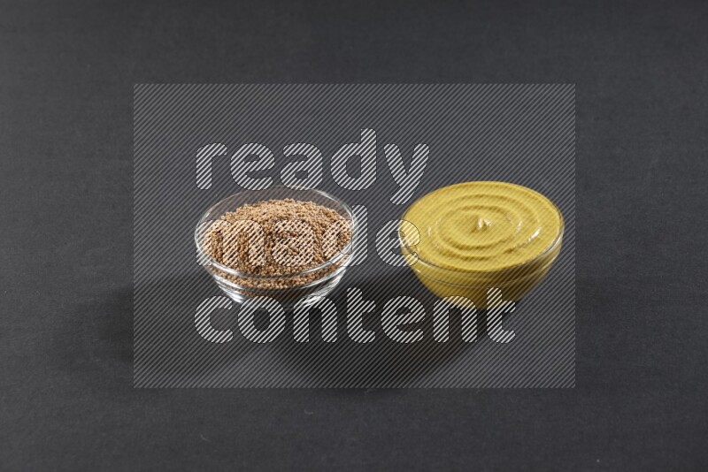 وعاءان زجاجيان إحداهما ممتلئ ببذور الخردل والأخر ممتلئ بمعجون الخردل علي خلفية سوداء