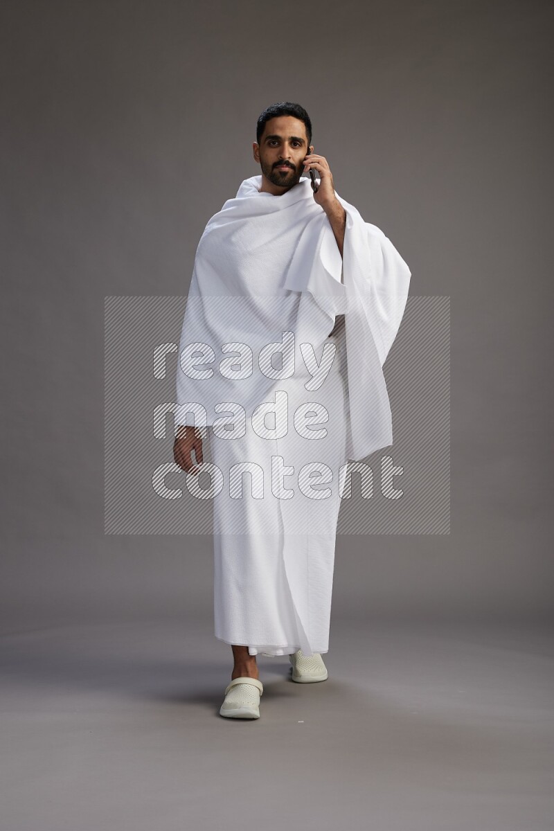 A man wearing Ehram Standing talking on phone on gray background
