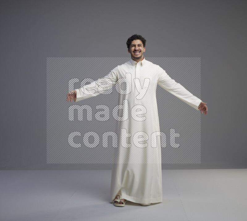 A Saudi man standing wearing thob interacting with the camera on gray background