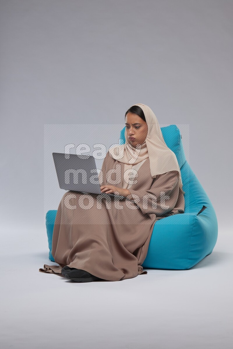 A Saudi woman sitting on a blue beanbag and working on laptop