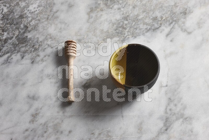 Multicolored pottery bowl with wooden honey dipper on the side on grey marble background