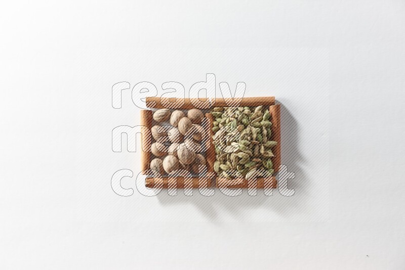 مربعان من أعواد القرفة ممتلئان بحبوب الهيل وجوزة الطيب علي خلفية بيضاء