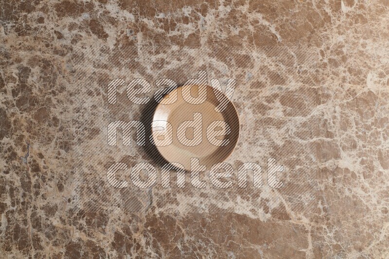 A beige pottery plate on beige marble background