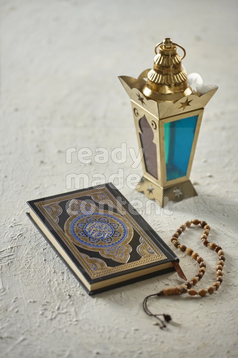 A golden lantern with different drinks, dates, nuts, prayer beads and quran on textured white background