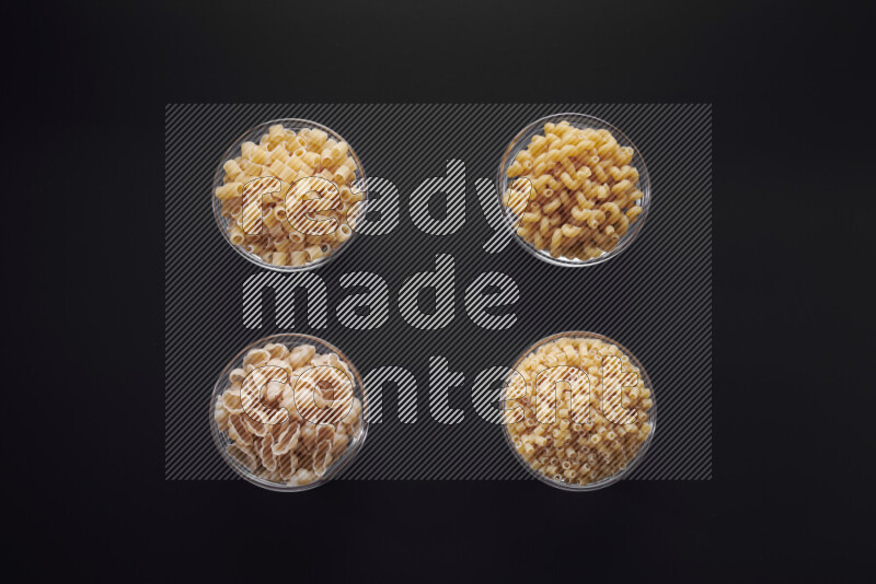 Different pasta types in glass bowls on black background