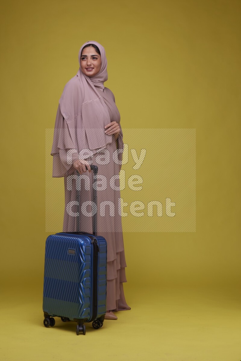 A woman With suit Case on a Yellow Background wearing Brown Abaya with Hijab