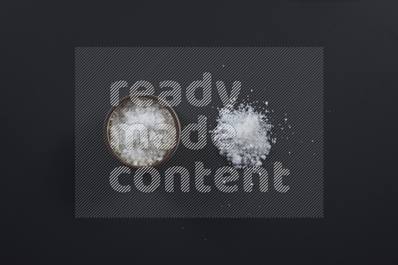 وعاء فخاري ممتلئ بملح الطعام الناعم وملح البحر الخشن على خلفية سوداء