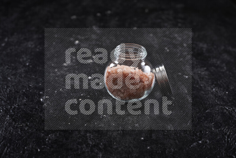A glass jar full of coarse himalayan salt crystals on black background