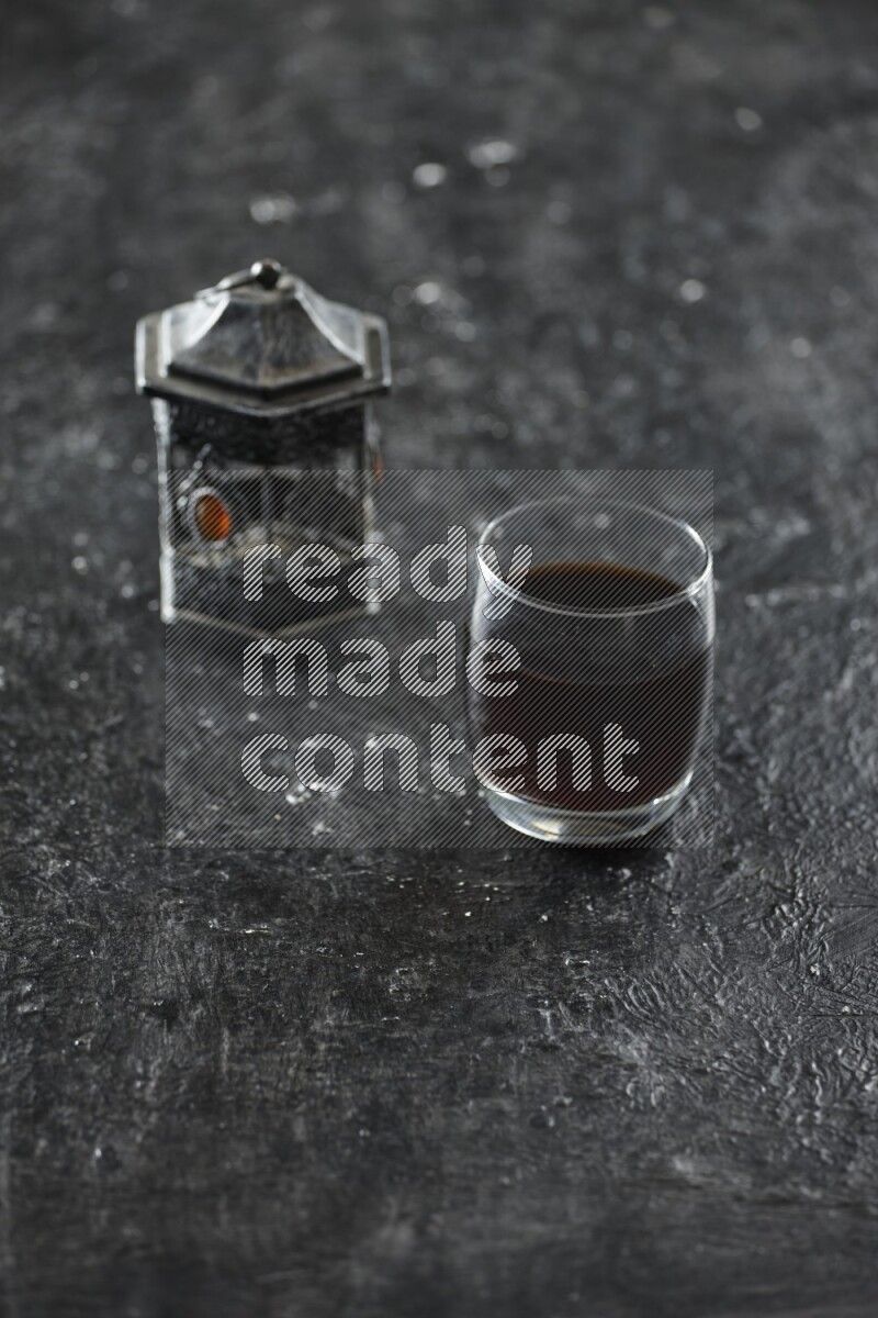 A silver lantern with different drinks, dates, nuts, prayer beads and quran on textured black background