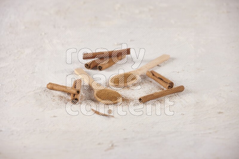 Two wooden spoons full of cinnamon powder with cinnamon sticks on white background