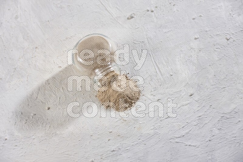 A glass spice jar full of garlic powder flipped over with the powder came out on a textured white flooring