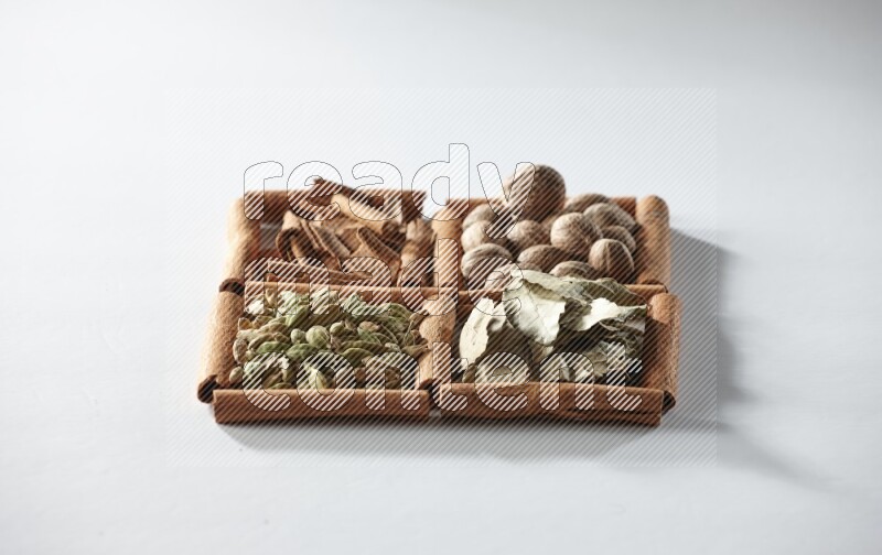 4 مربعات من أعواد القرفة ممتلئة بجوزة الطيب وأوراق الغار وحبوب الهيل والقرفة على أرضية بيضاء