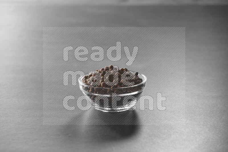A glass bowl full of allspice on black flooring