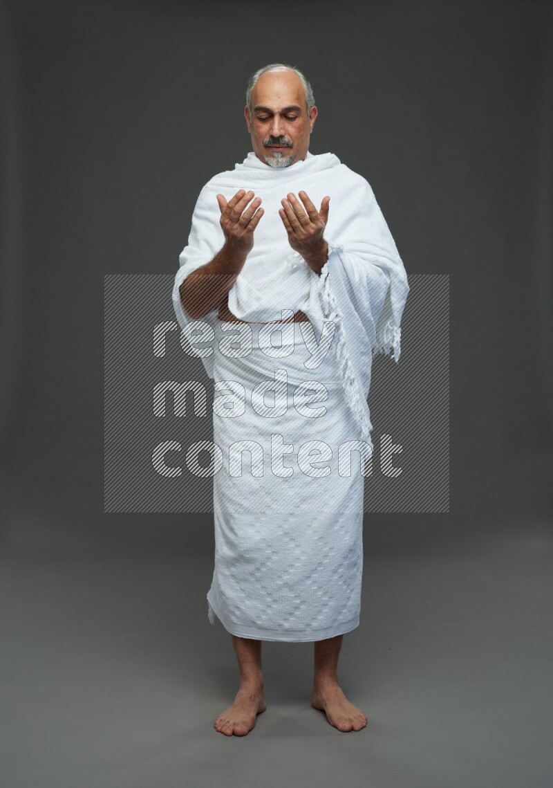 A man wearing Ehram Standing dua'a on gray background