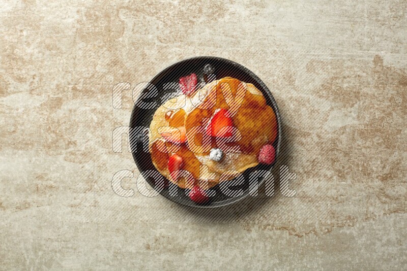 Three stacked mixed berries pancakes in a black plate on beige background