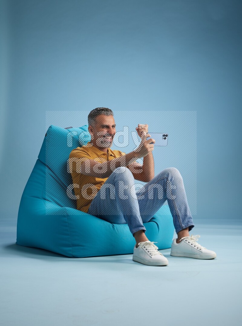 A man sitting on a blue beanbag and playing on phone