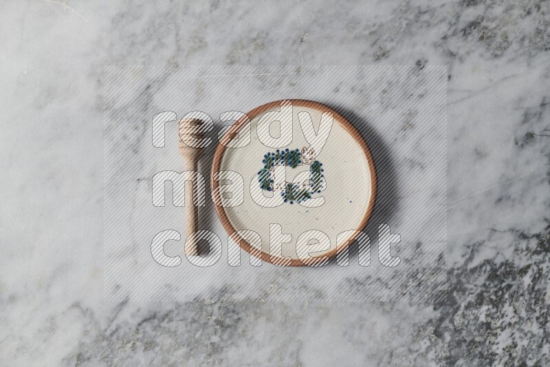 Decorative pottery plate with wooden honey dipper on the side on grey marble background