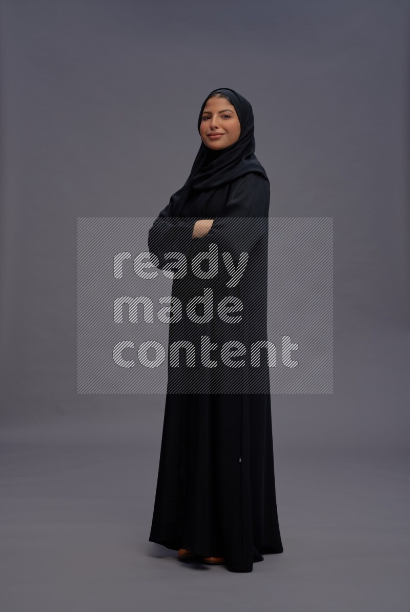 Saudi woman wearing Abaya standing with crossed arms on gray background