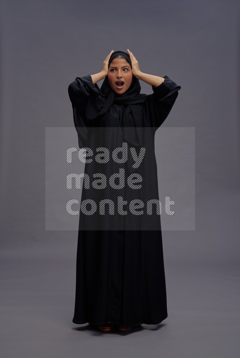 Saudi woman wearing Abaya standing hands behind head on gray background