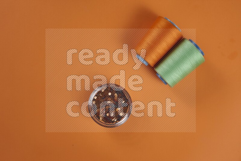 A green and orange collection of sewing and tailoring tools arranged on a orange background