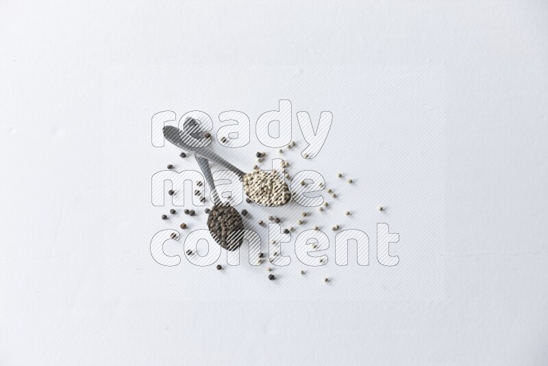 2 metal spoons full of black and white pepper beads with spreaded beads on white flooring