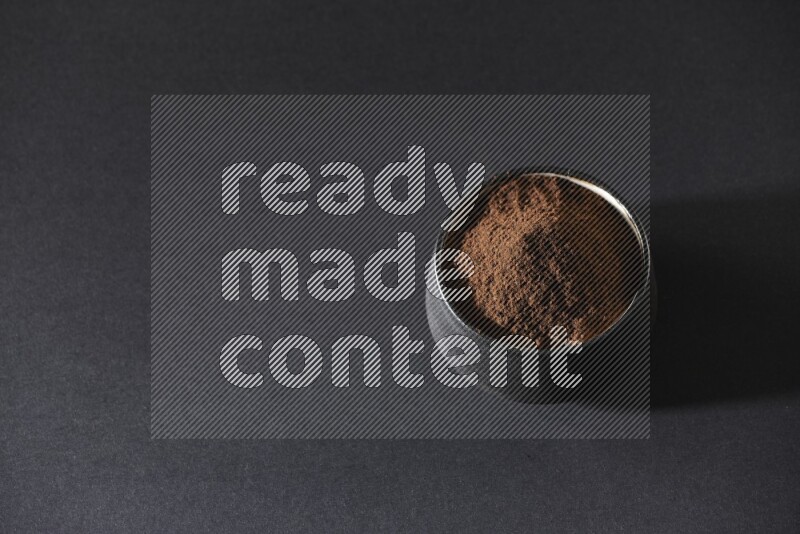 A black pottery bowl full of cloves powder on a black flooring