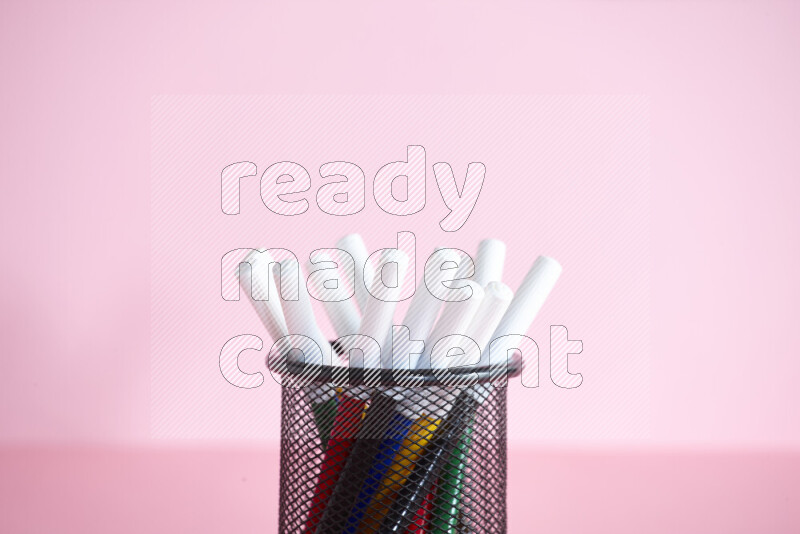 Pens, pencils and other different school supplies in a metal pen holder on rose background
