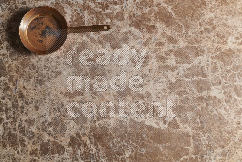 A small copper pan on beige marble background