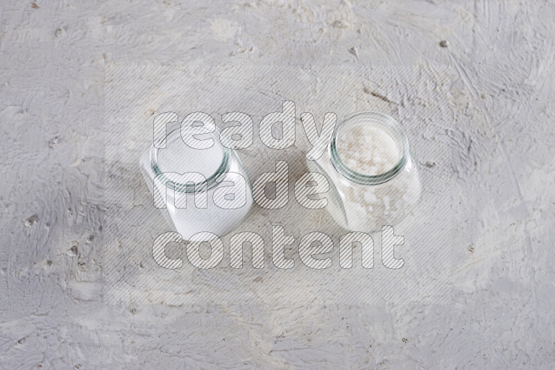 2 glass jars one is filled with table salt and the other with coarse sea salt on white background