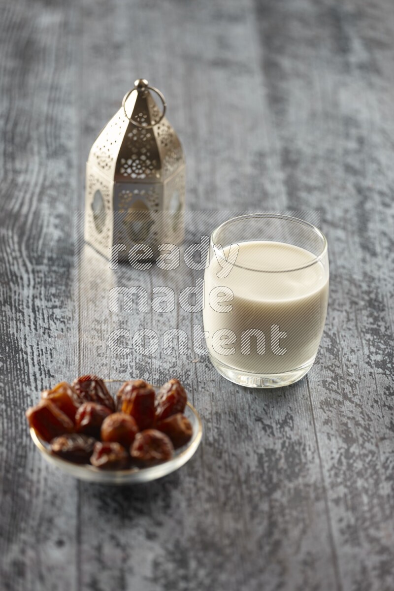 A silver lantern with different drinks, dates, nuts, prayer beads and quran on grey wooden background