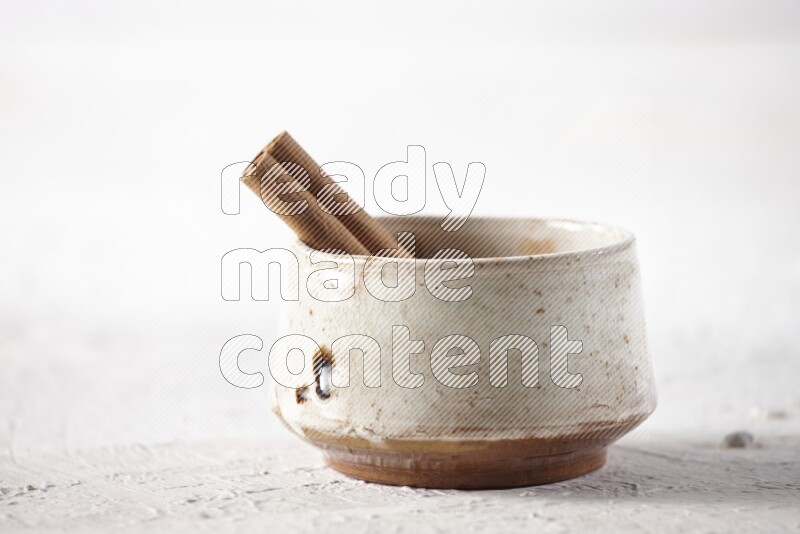 Ceramic beige bowl full of cinnamon powder with a cinnamon stick on a textured white background
