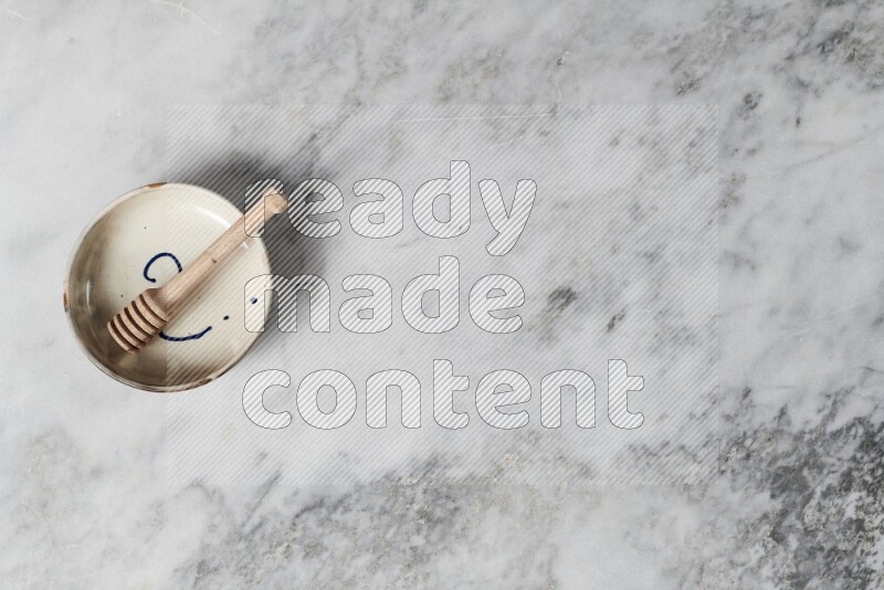Multicolored pottery bowl with wooden honey dipper in it on grey marble background