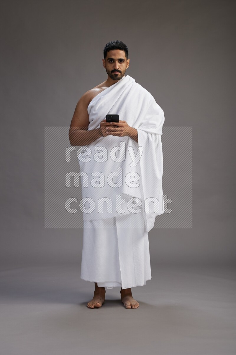 A man wearing Ehram Standing texting on phone on gray background
