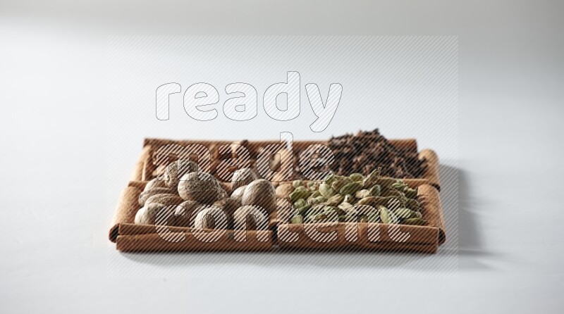 4 مربعات من أعواد القرفة ممتلئة بالهيل والقرفة والقرنفل وجوزة الطيب على أرضية بيضاء