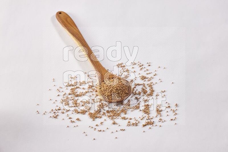 A wooden ladle full of mustard seeds on a white flooring
