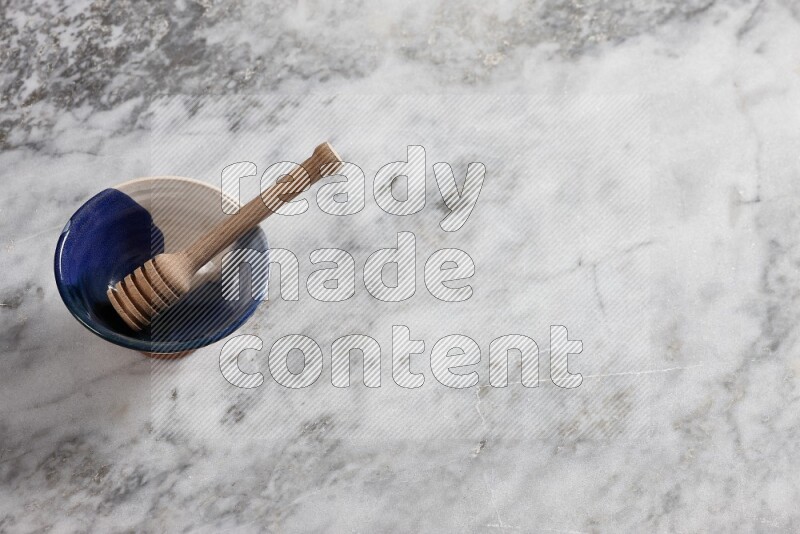 Multicolored pottery bowl with wooden honey dipper in it on grey marble background
