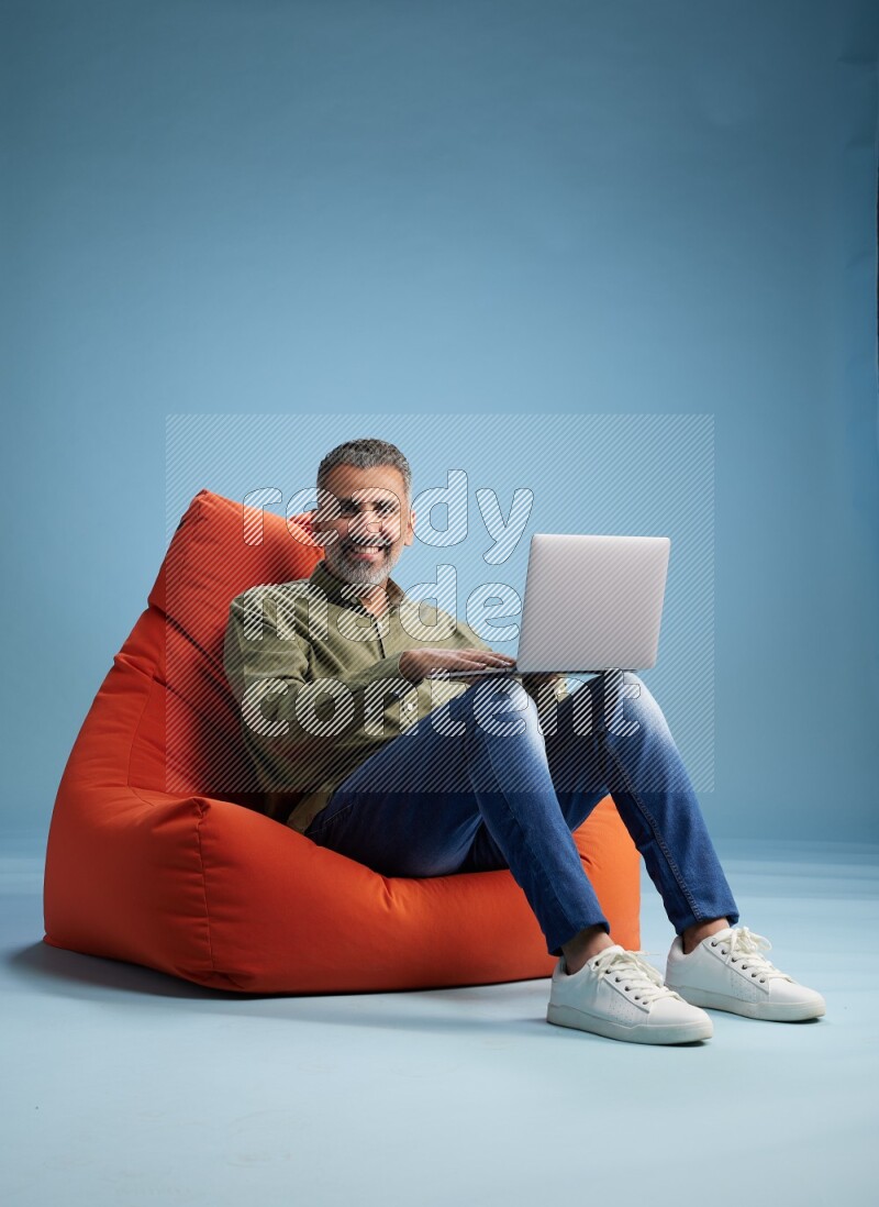 A man sitting on an orange beanbag and working on laptop