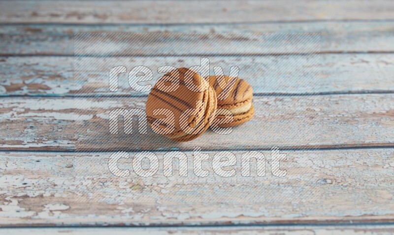 45º Shot of two light brown Almond Cream macarons on light blue wooden background
