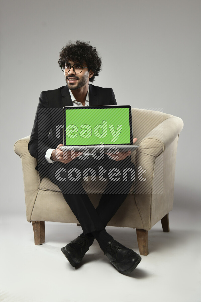 A man wearing formal sitting on a chair showing a laptop screen on white background