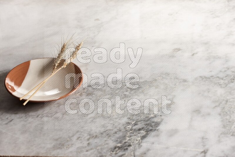 Wheat stalks on multicolored pottery plate on grey marble background