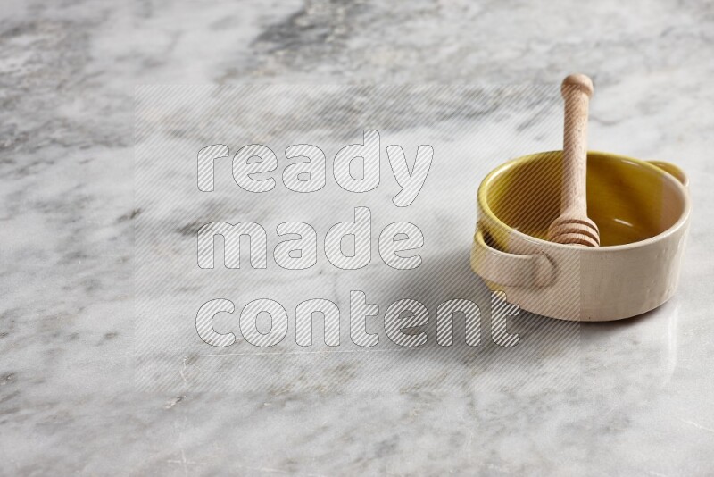 Multicolored pottery bowl with wooden honey dipper in it on grey marble background