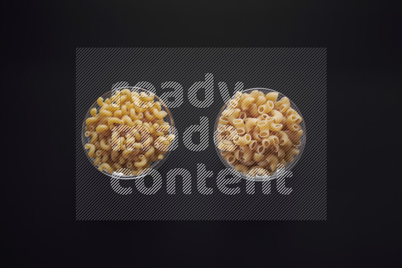 Different pasta types in glass bowls on black background