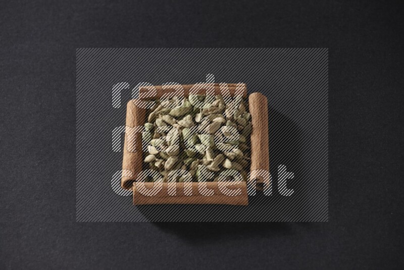 A single square of cinnamon sticks full of Cardamom on black flooring