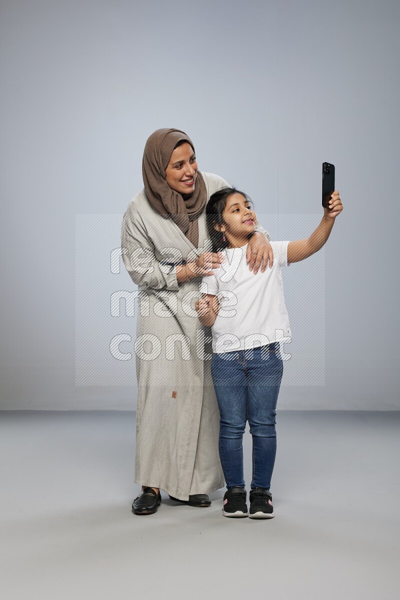 A girl standing taking selfie with her mother on gray background